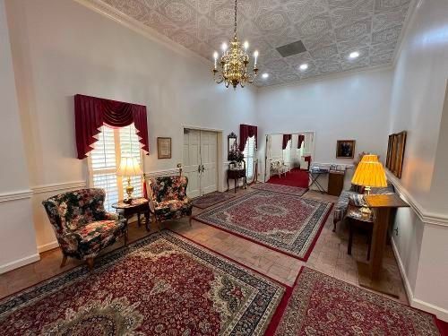 A well-lit room with ornate rugs, patterned armchairs, and a chandelier; doors and windows are visible.