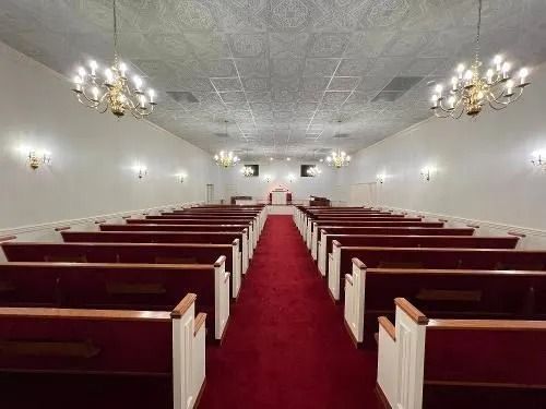 Interior view of a church sanctuary with rows of pews facing an altar, red carpet, and chandeliers.