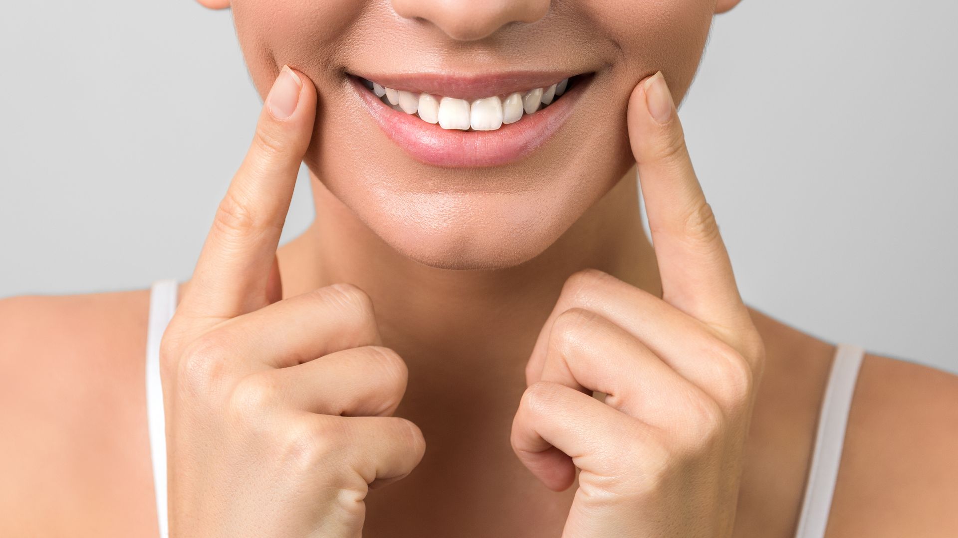Close-up of a smiling woman with white teeth, with her fingers pointed on each cheek.