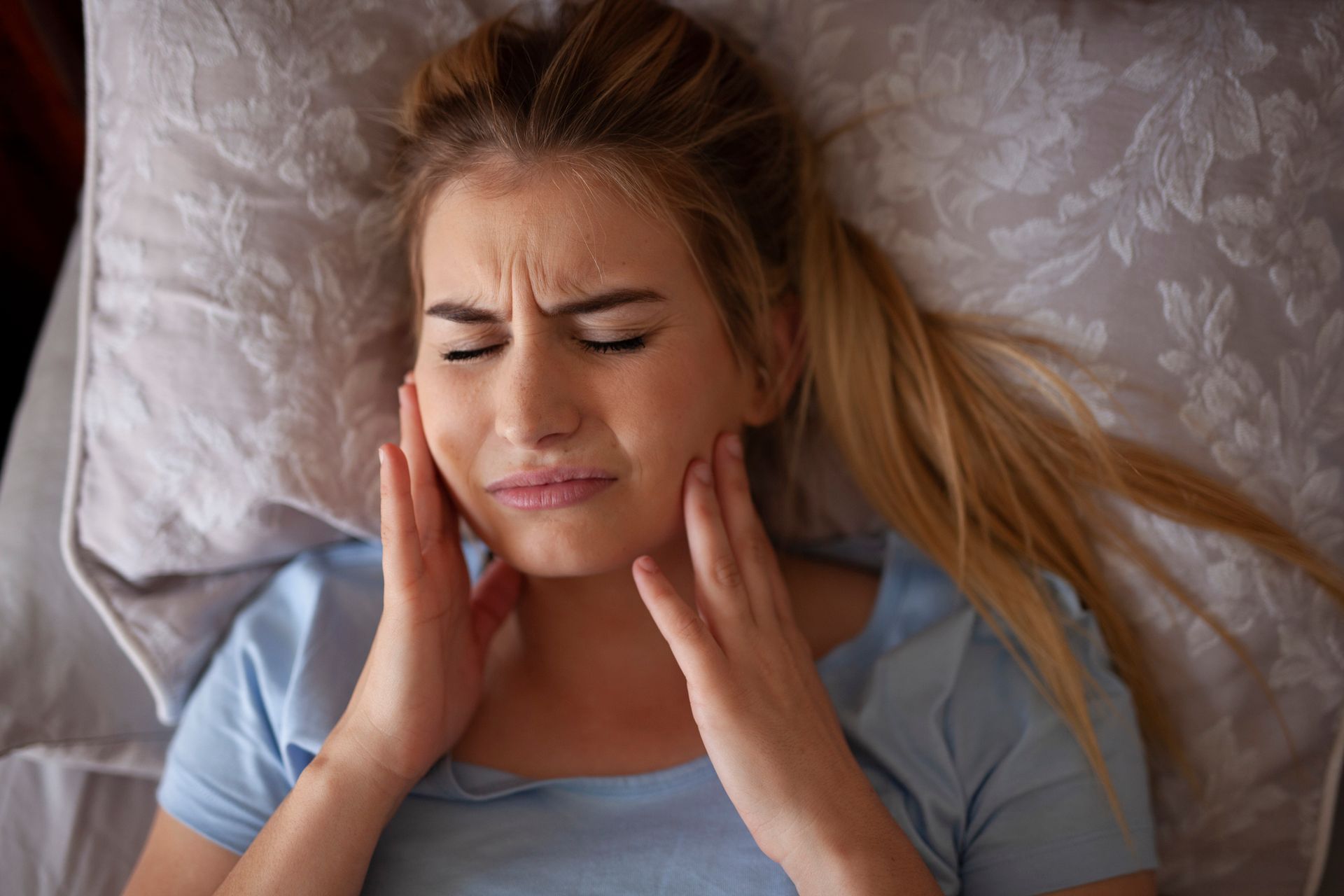 A woman in bed with hands on cheeks, showing pain.