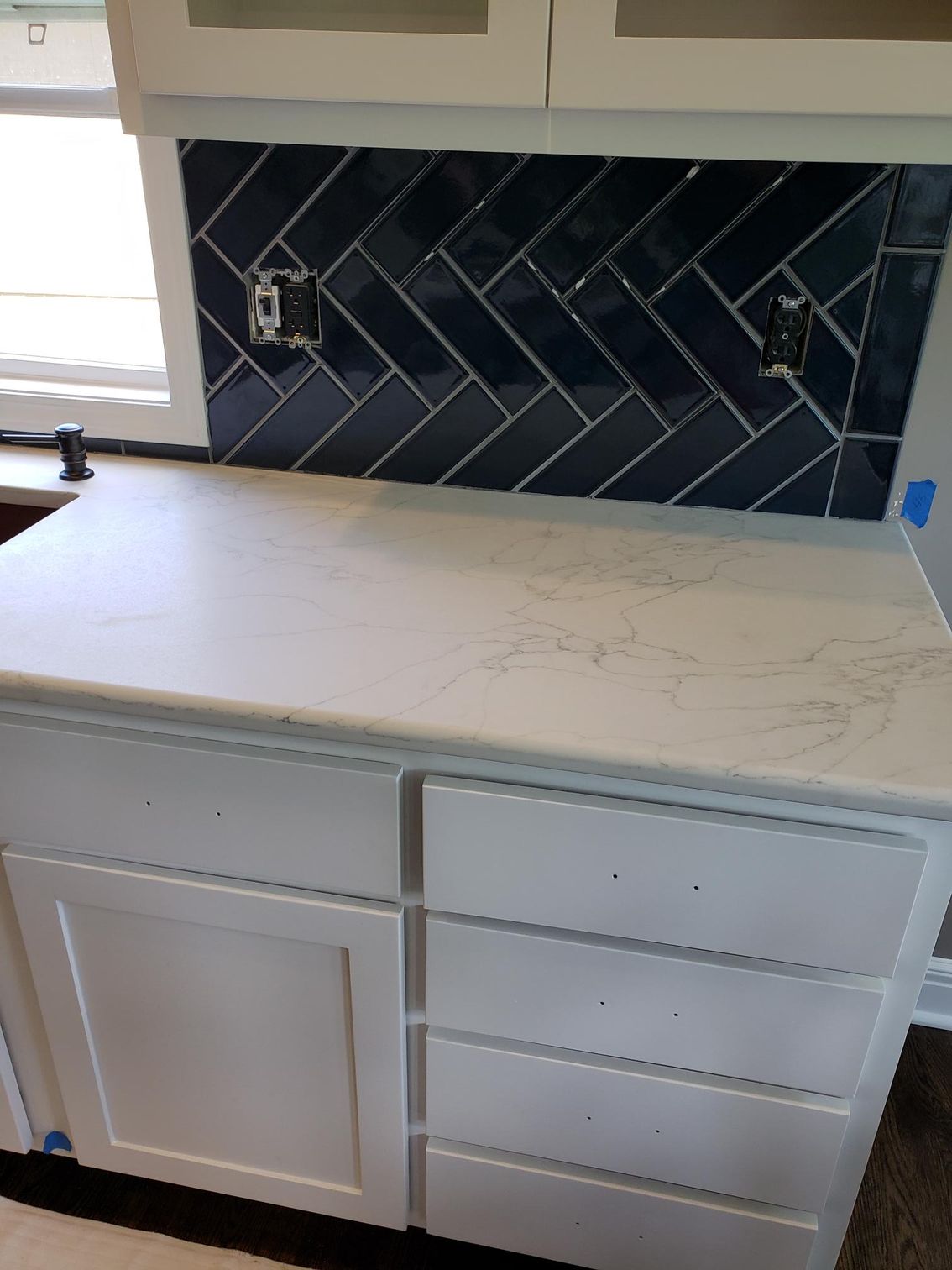 A kitchen counter with white cabinets and blue tiles.