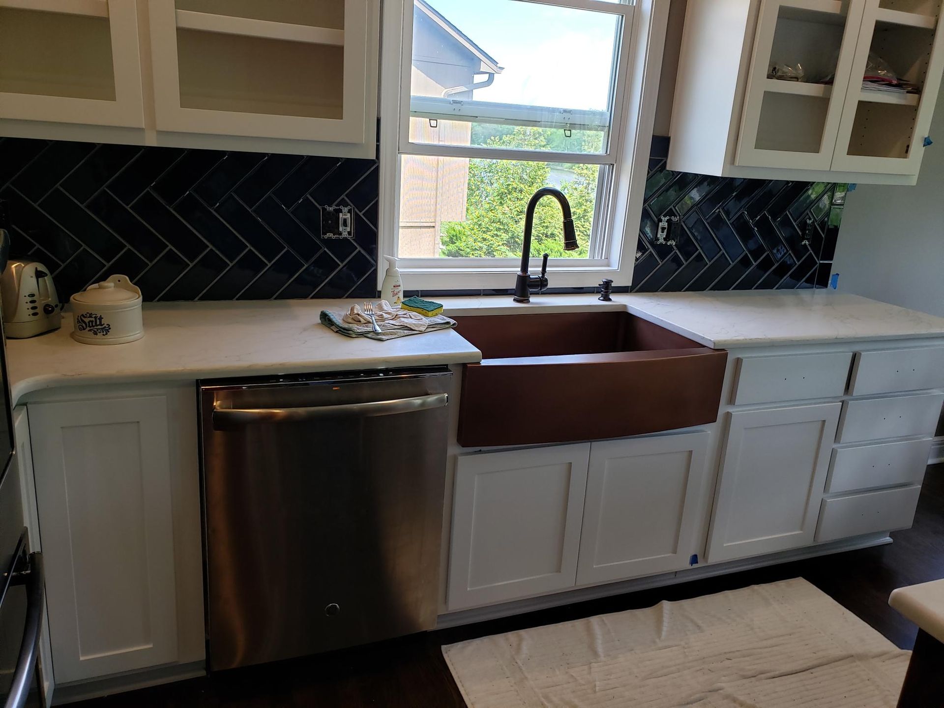 A kitchen with a copper sink , stainless steel dishwasher , and white cabinets.