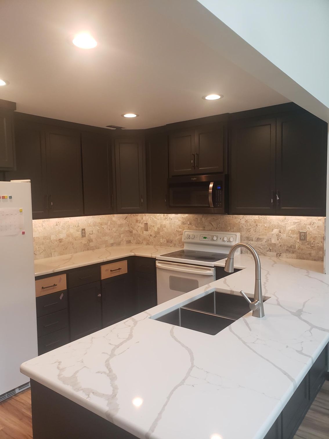 A kitchen with black cabinets , white counter tops , a stove and a sink.