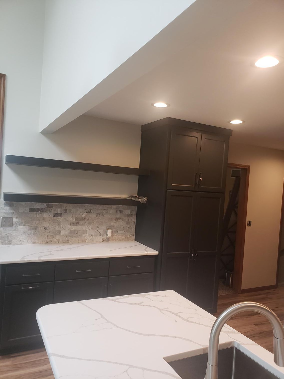 A kitchen with black cabinets , white counter tops , and a sink.