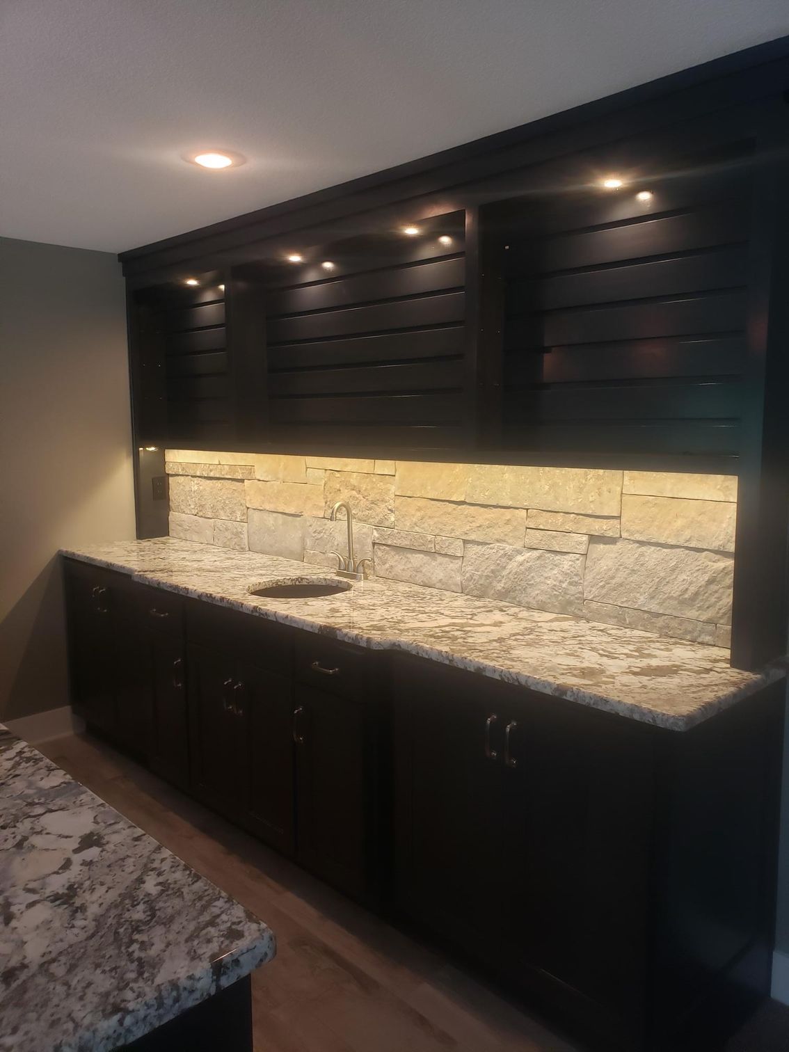 A kitchen with granite counter tops , black cabinets , and a sink.