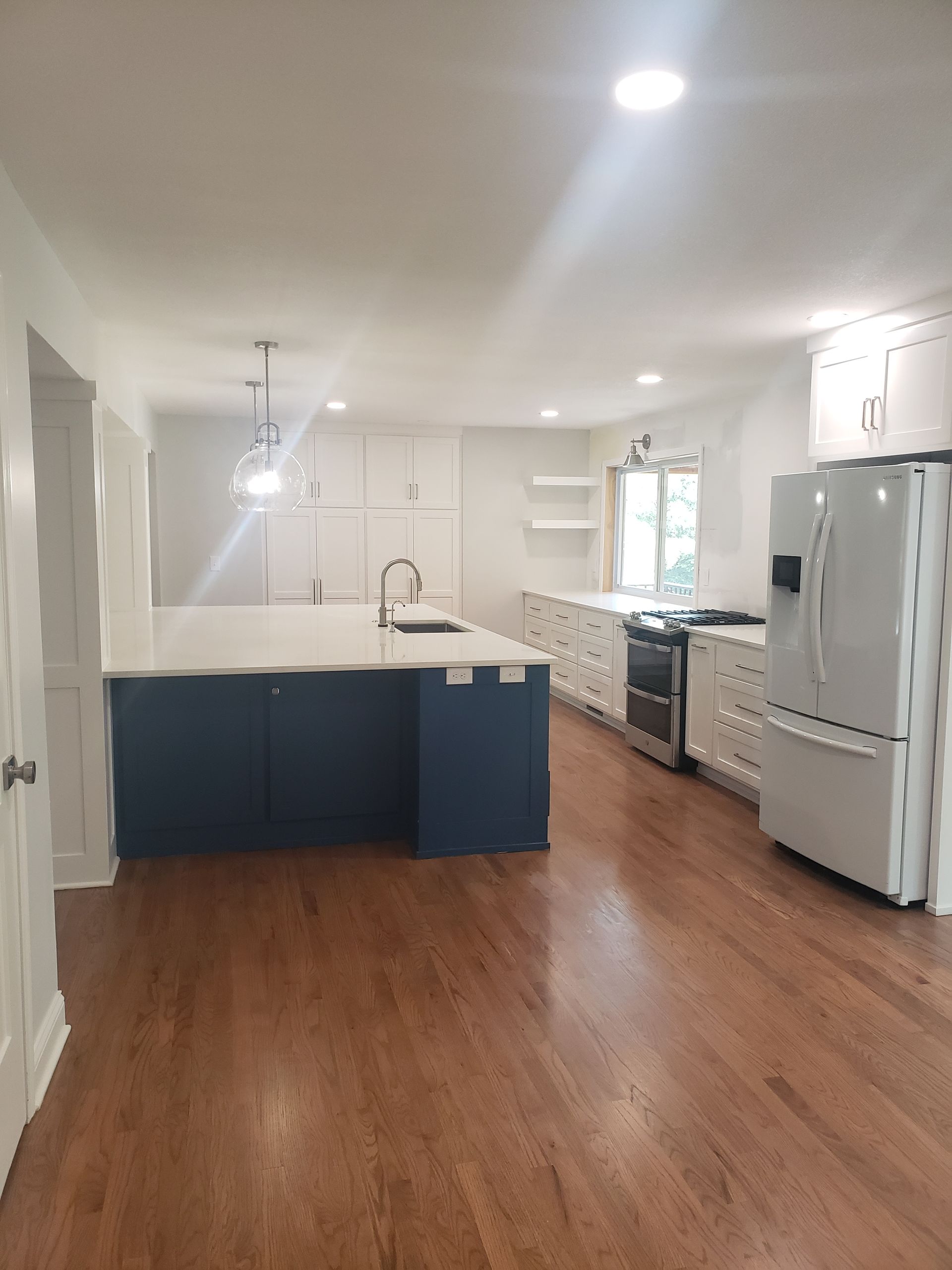 A kitchen with blue cabinets , white cabinets , a refrigerator , stove and sink.