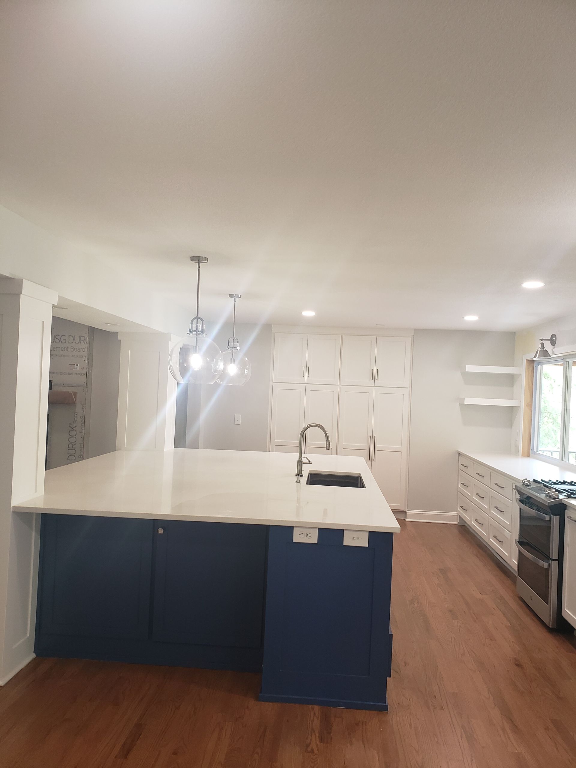 A kitchen with blue cabinets , white counter tops , and hardwood floors.
