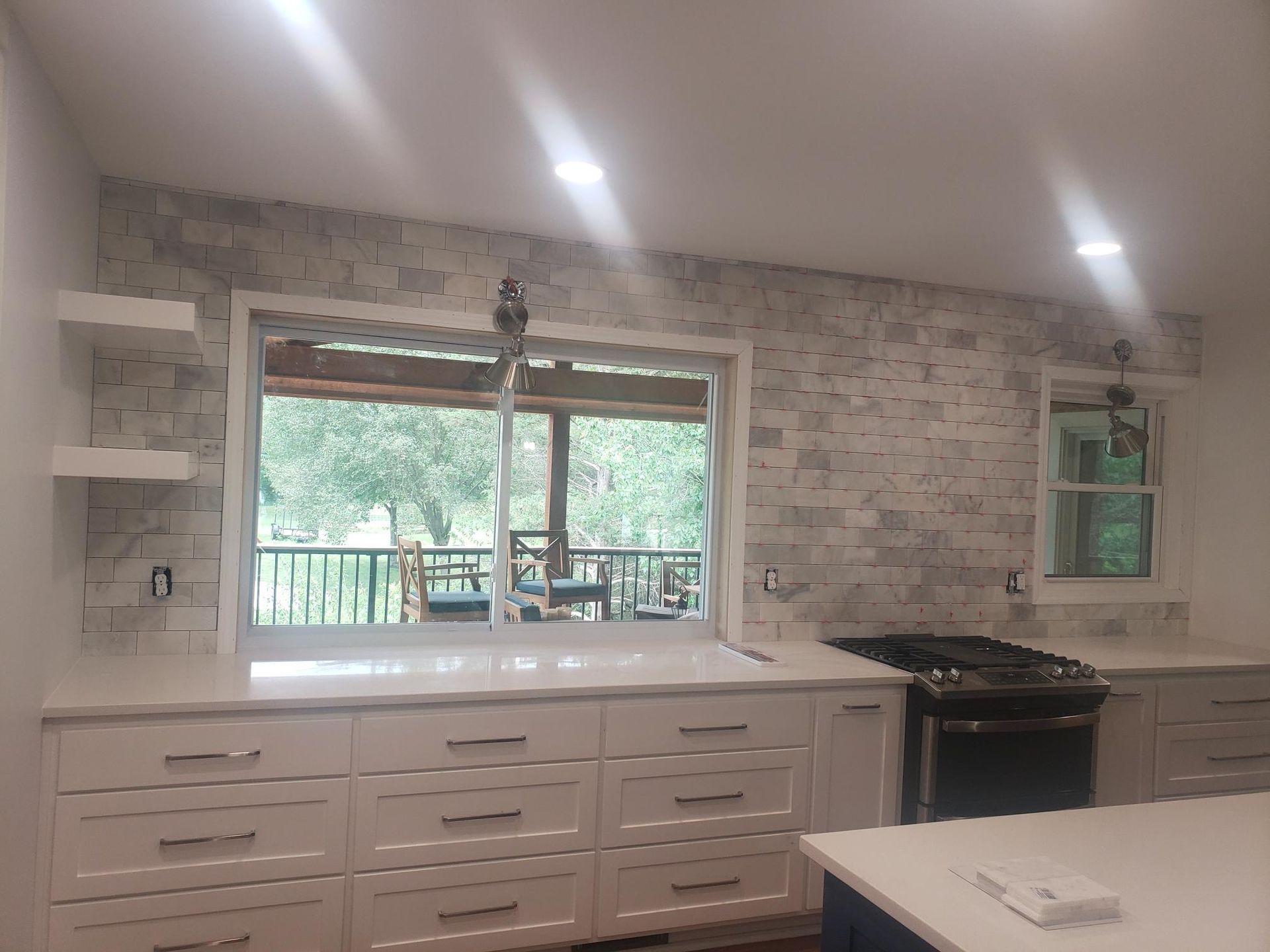 A kitchen with white cabinets and a large window with a view of a deck.