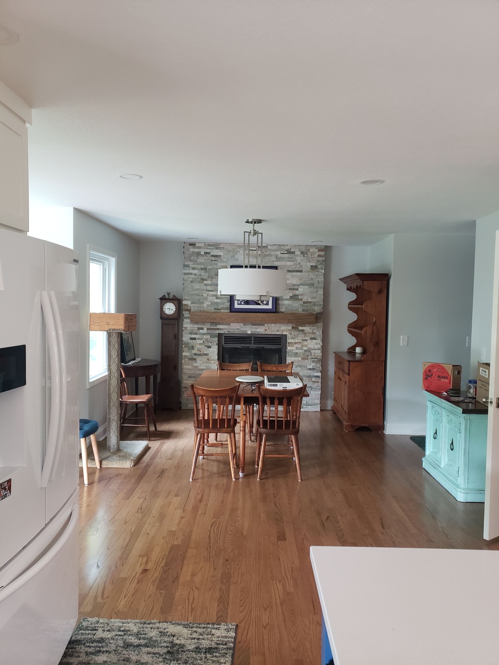 A living room with a dining table and chairs , a fireplace , and a refrigerator.