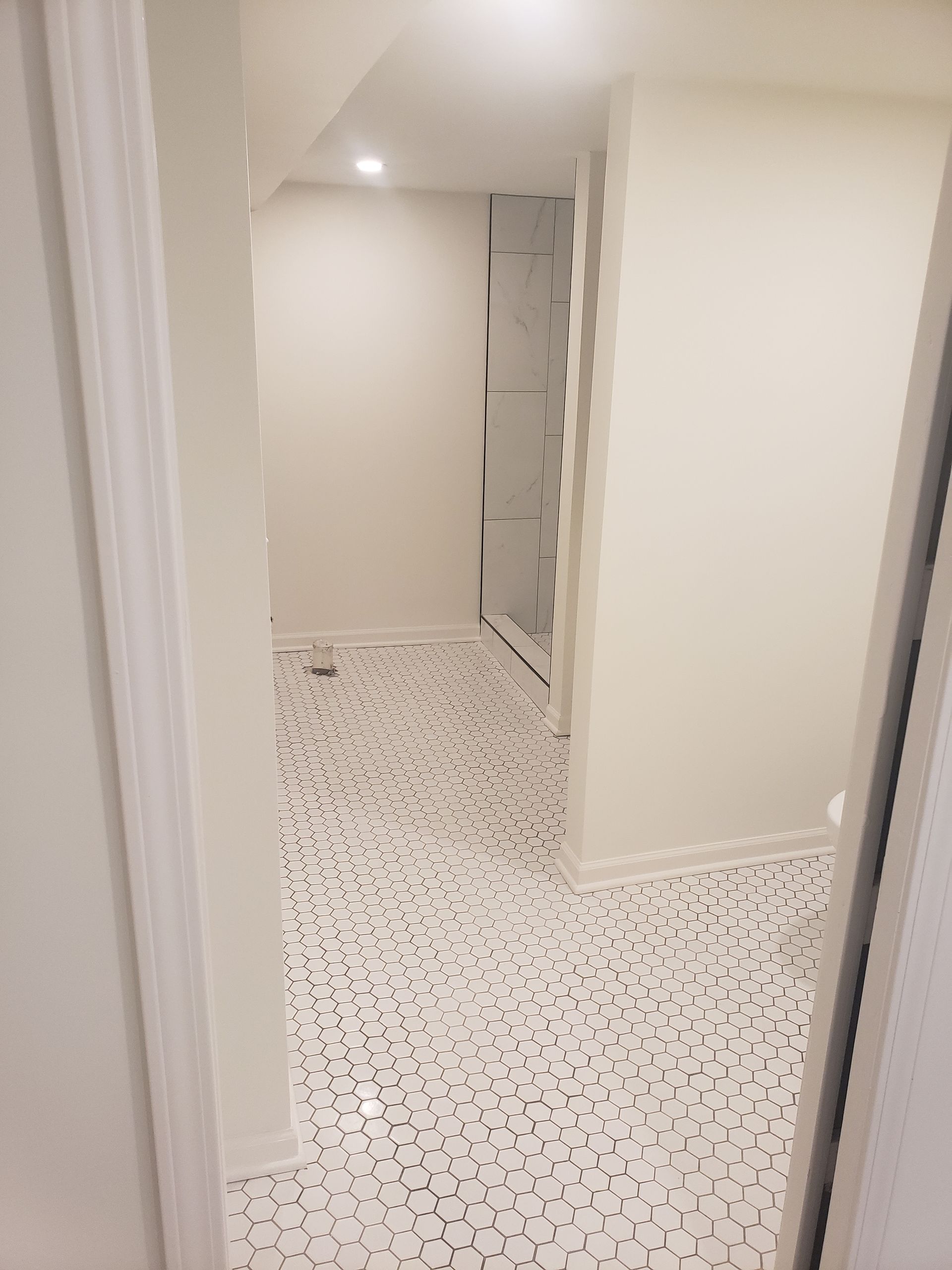 A hallway in a basement with a white tile floor and white walls.