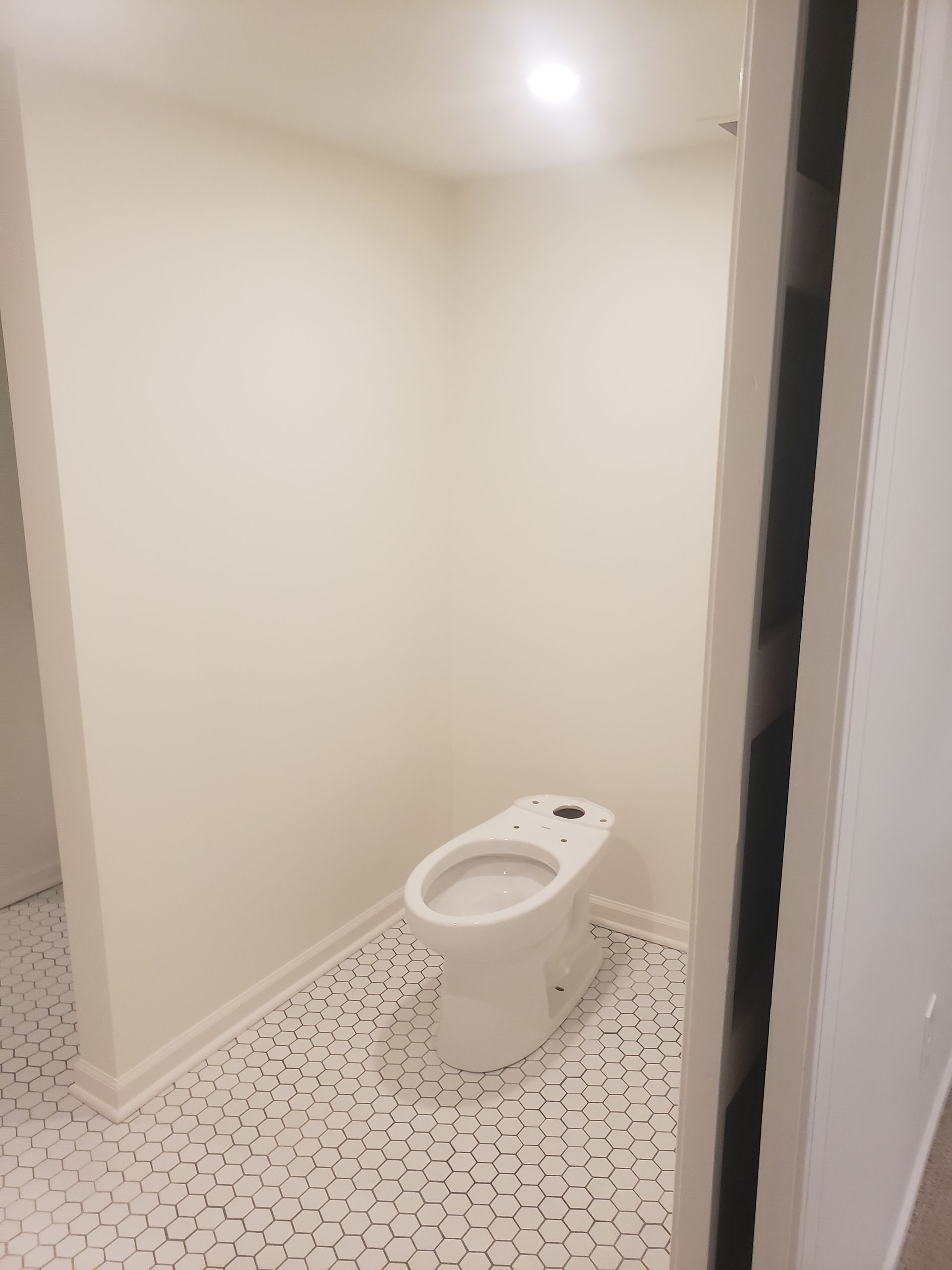 A white toilet is sitting in a bathroom next to a white wall.