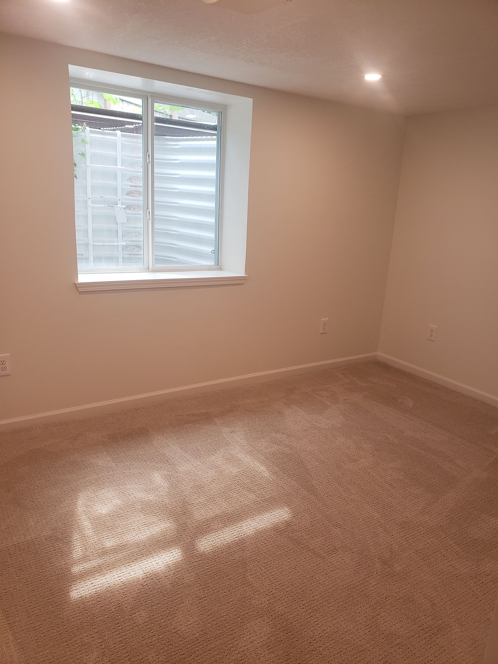 An empty room with a window and a carpeted floor.