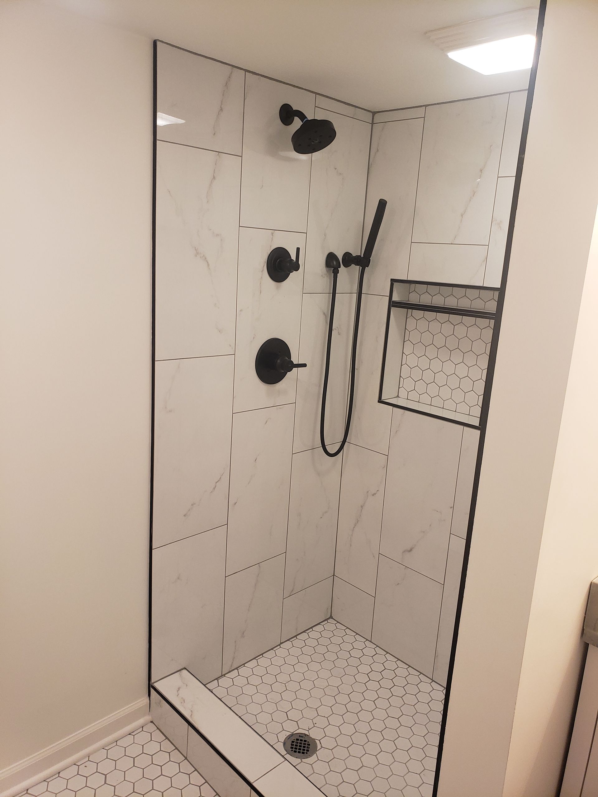 A bathroom with a walk in shower with a black shower head.