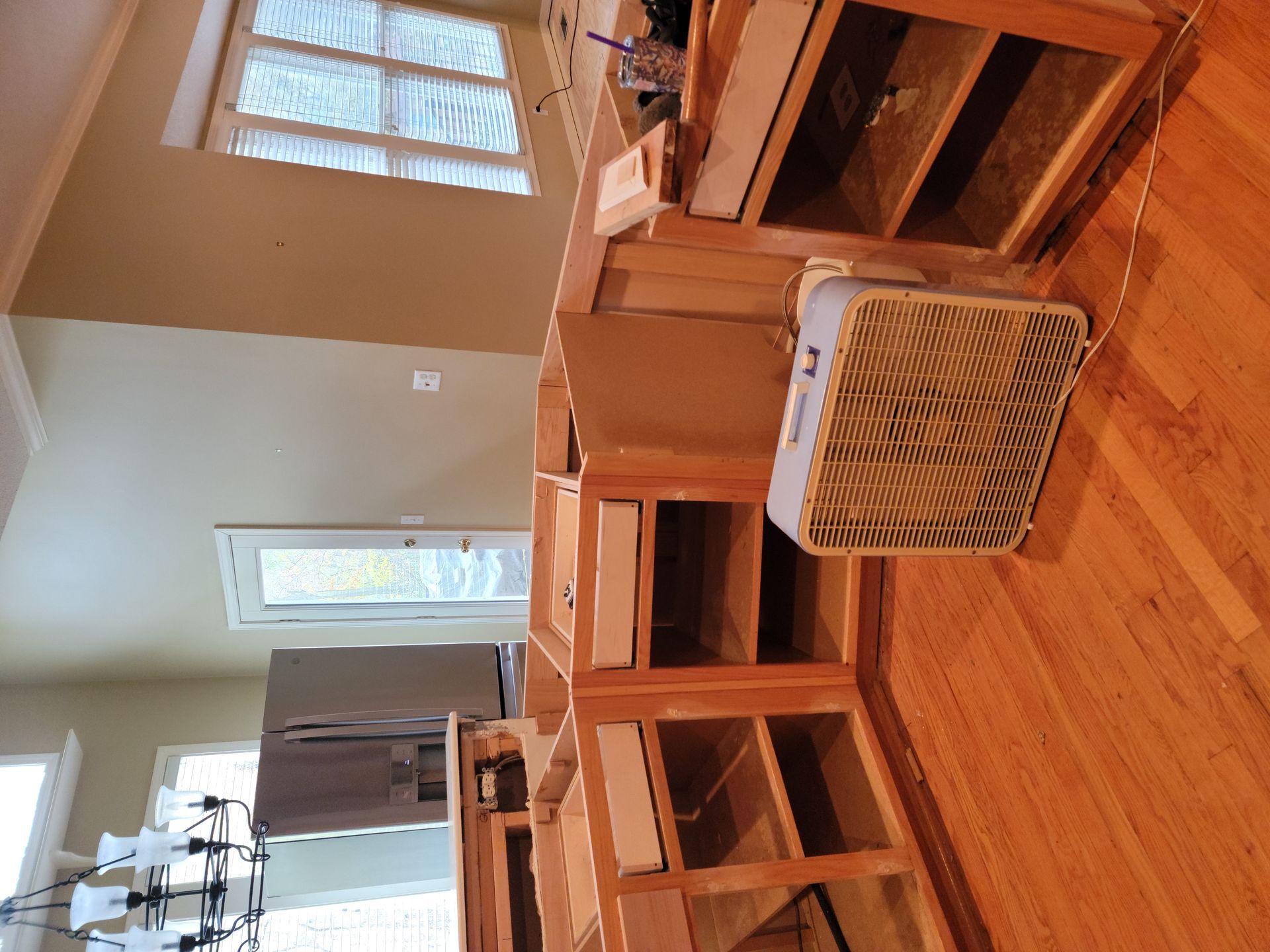 A fan is sitting on a wooden floor in a kitchen.