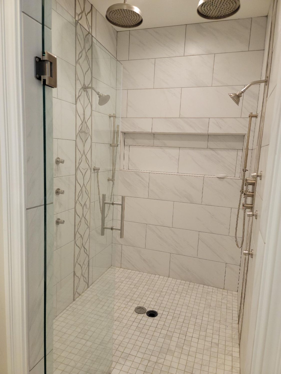 A walk in shower with two shower heads and a glass door.