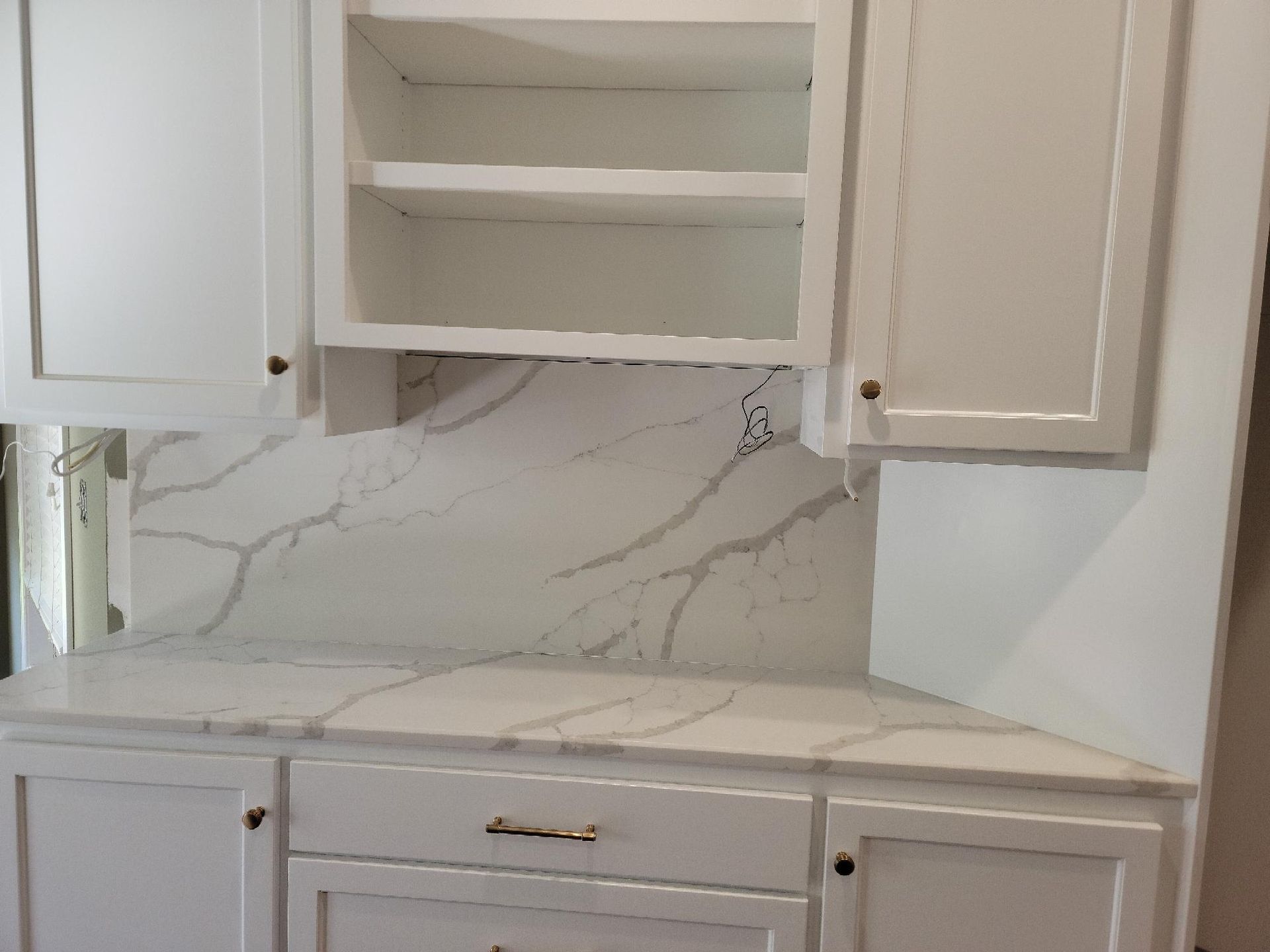 A kitchen with white cabinets and marble counter tops.