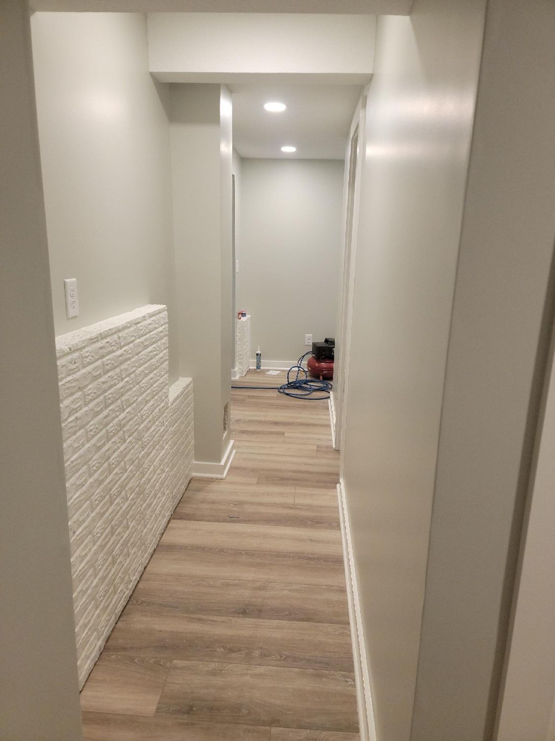 A long hallway with a wooden floor and white brick walls.