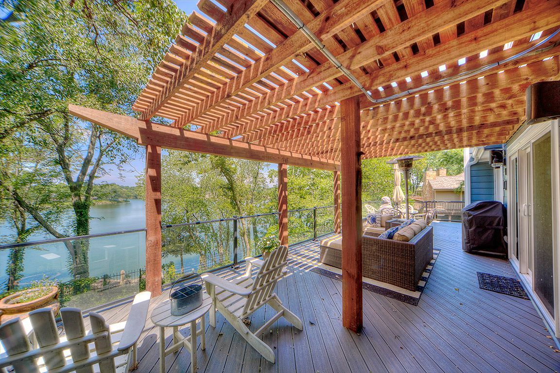 A wooden deck with a pergola overlooking a lake.