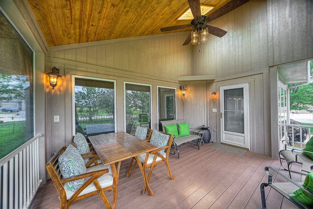 A screened in porch with a table and chairs and a ceiling fan.