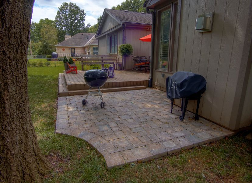 A patio with a grill and umbrella in front of a house.