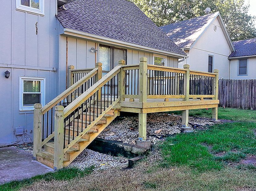 A wooden deck with stairs leading up to it is in the backyard of a house.