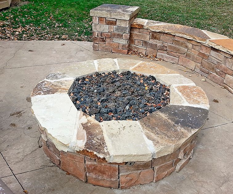 A stone fire pit is sitting on a patio next to a stone wall.