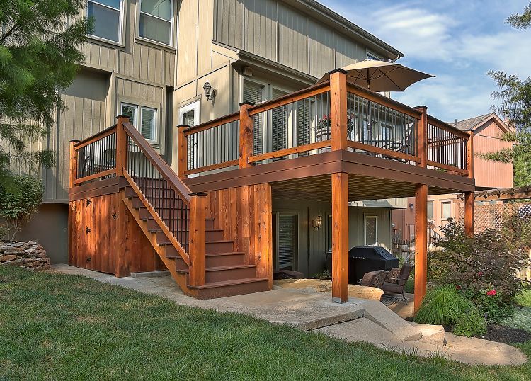 A large wooden deck with stairs leading up to it is in front of a house.