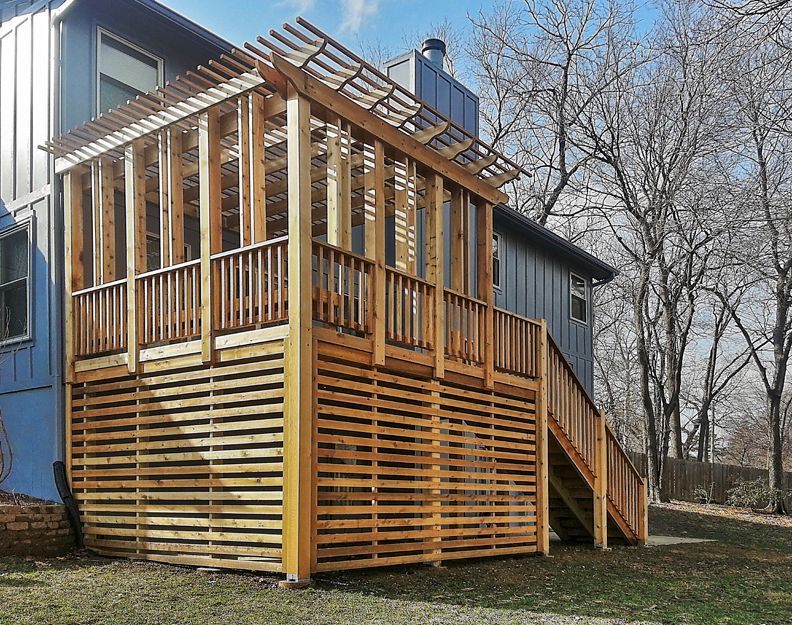 A wooden deck with stairs and a pergola on the side of a house.