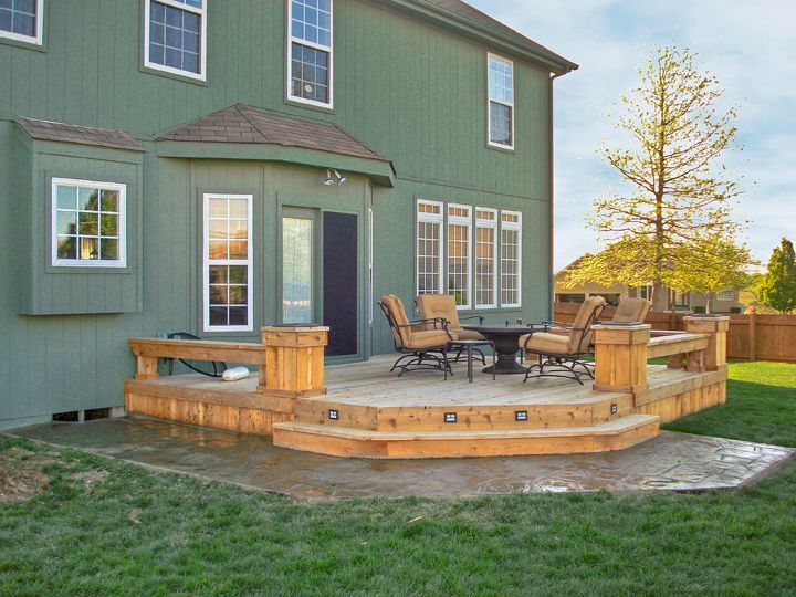 A green house with a wooden deck in front of it.