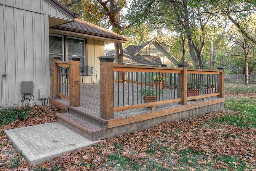 A wooden deck with a metal railing is in front of a house.