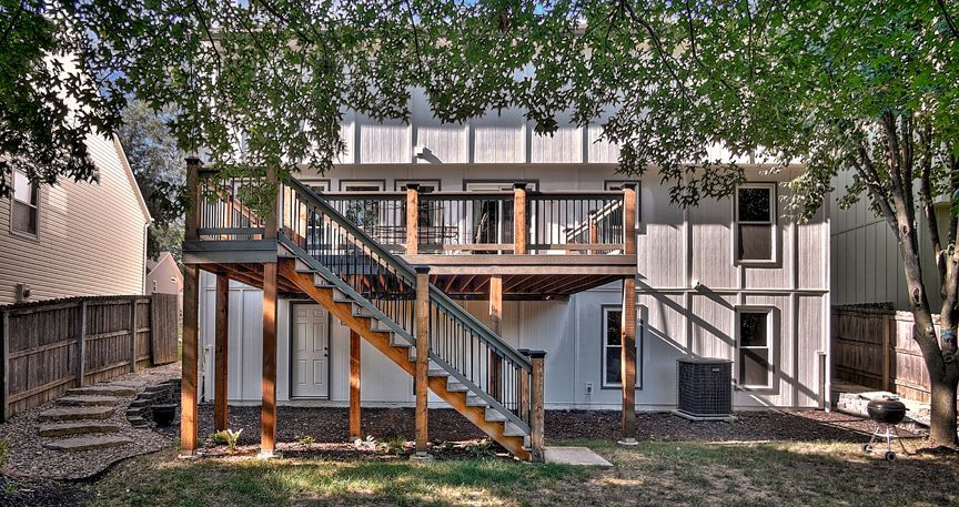 The back of a house with a large deck and stairs leading up to it.