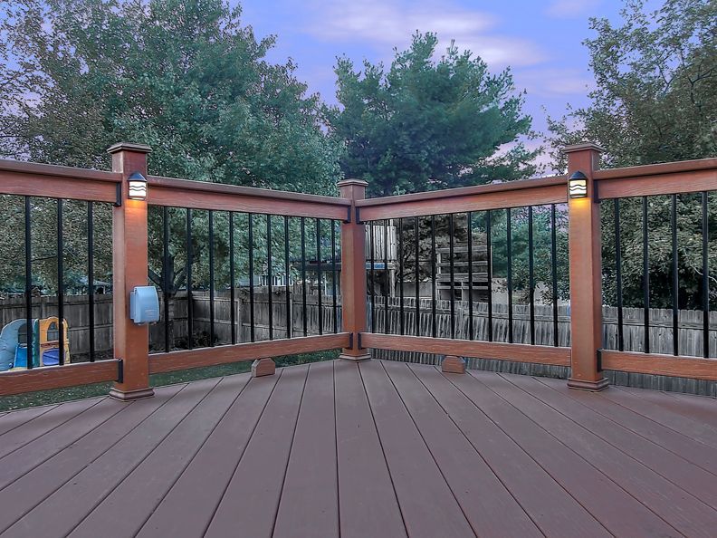 A wooden deck with a metal railing and trees in the background