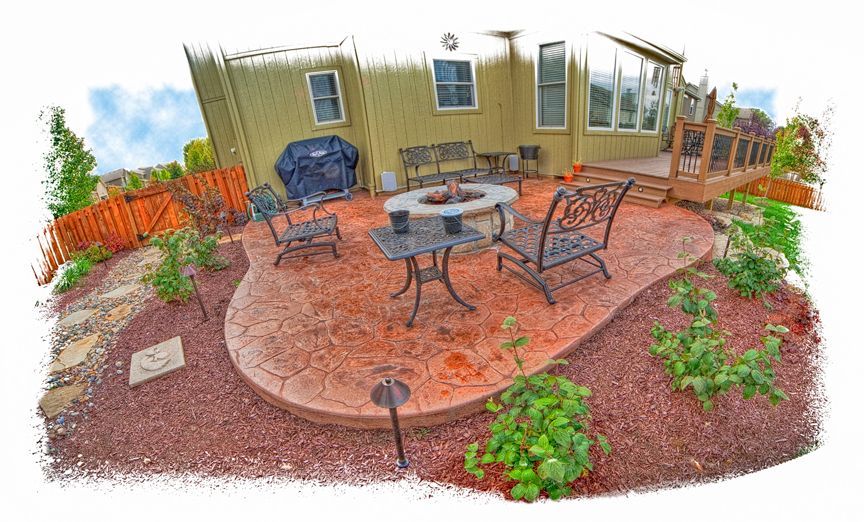 A patio with a table and chairs and a fire pit in front of a house.