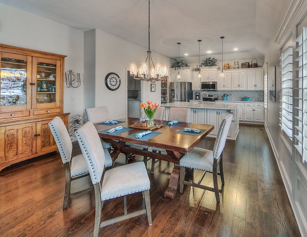 A dining room with a table and chairs and a kitchen in the background.