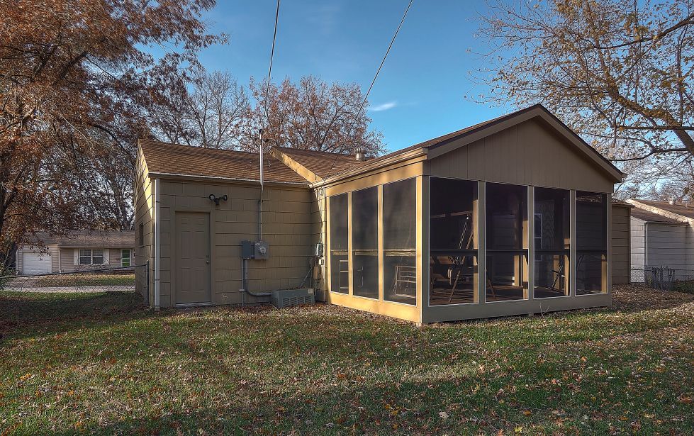 A screened in porch is in the backyard of a house.