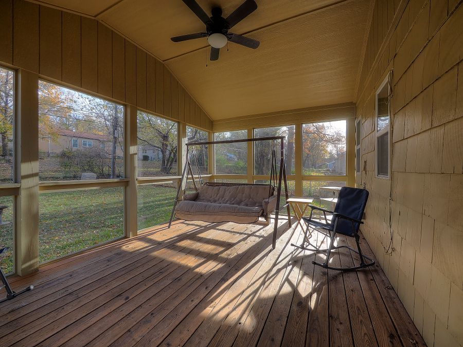 A screened in porch with a couch , rocking chairs and a ceiling fan.