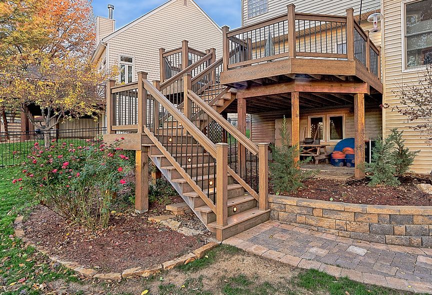 A wooden deck with stairs leading up to it in front of a house.