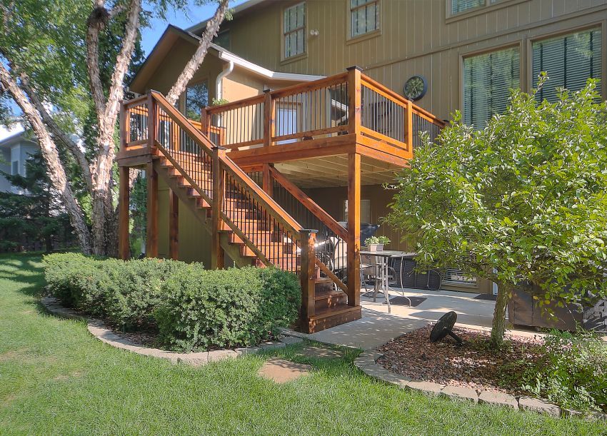 A wooden deck with stairs leading up to it is in the backyard of a house.