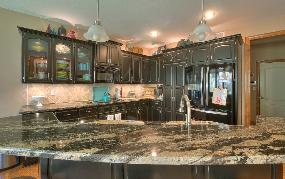 A kitchen with granite counter tops , black cabinets , a refrigerator and a sink.