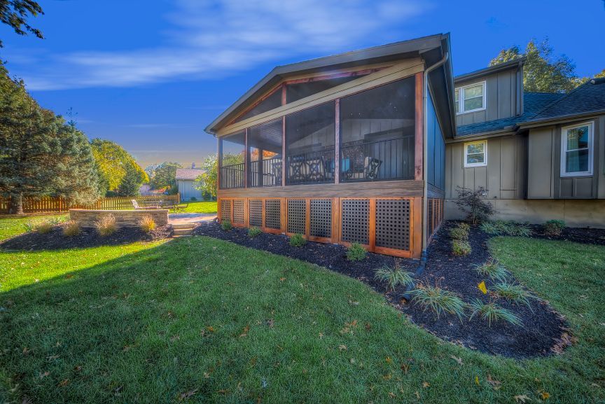 A house with a screened in porch and a large lawn in front of it.