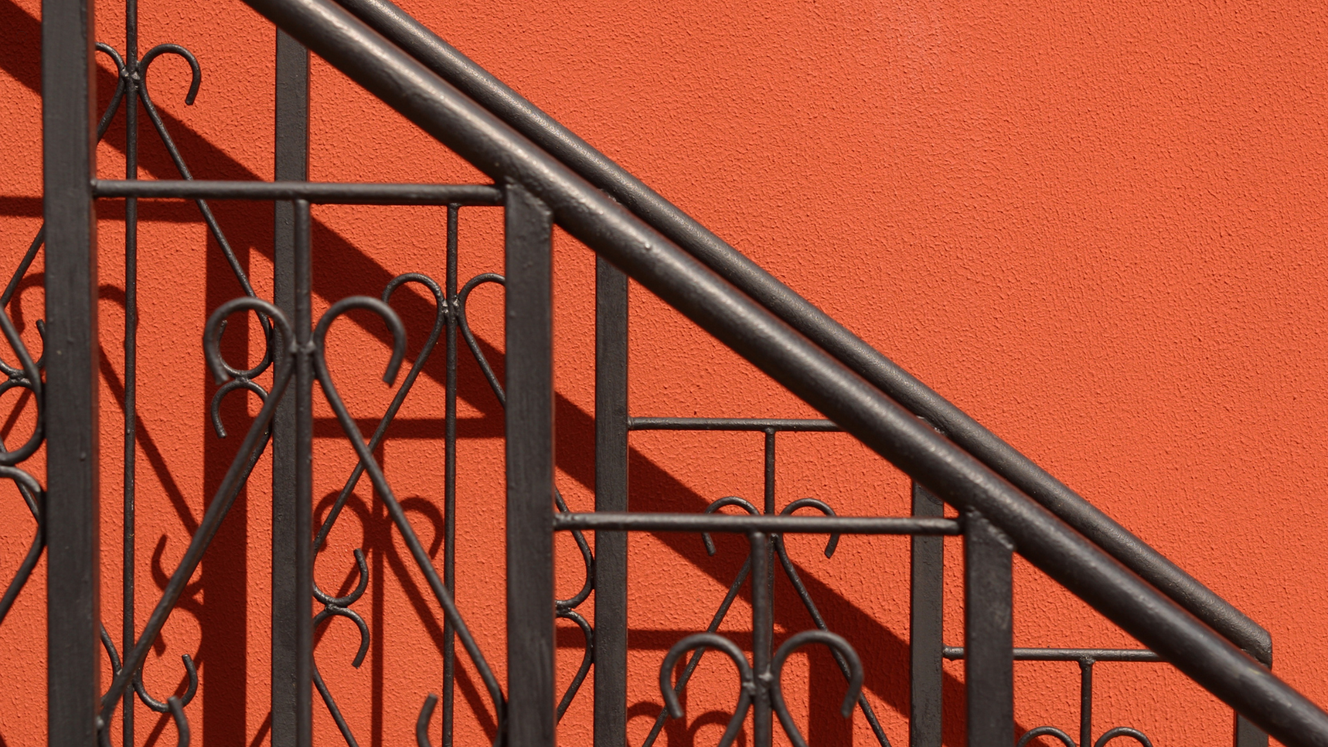 Red brick building with a wrought iron balcony. Black windows and decorative railing, white trim.