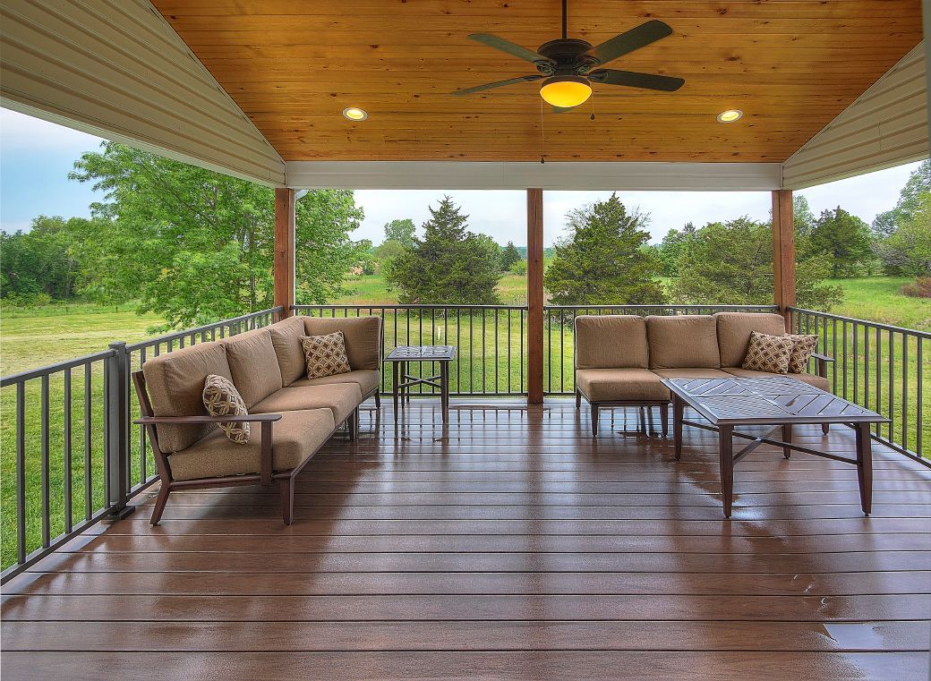 A porch with a couch , table , and ceiling fan.