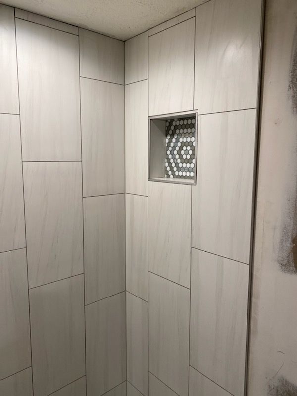 A bathroom with white tiles and a shelf in the corner.