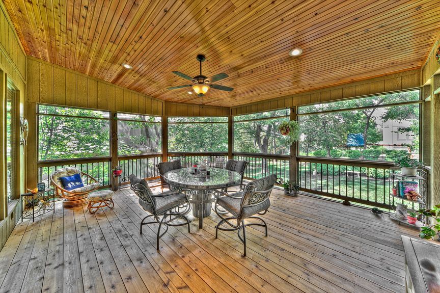 A screened in porch with a table and chairs and a ceiling fan.