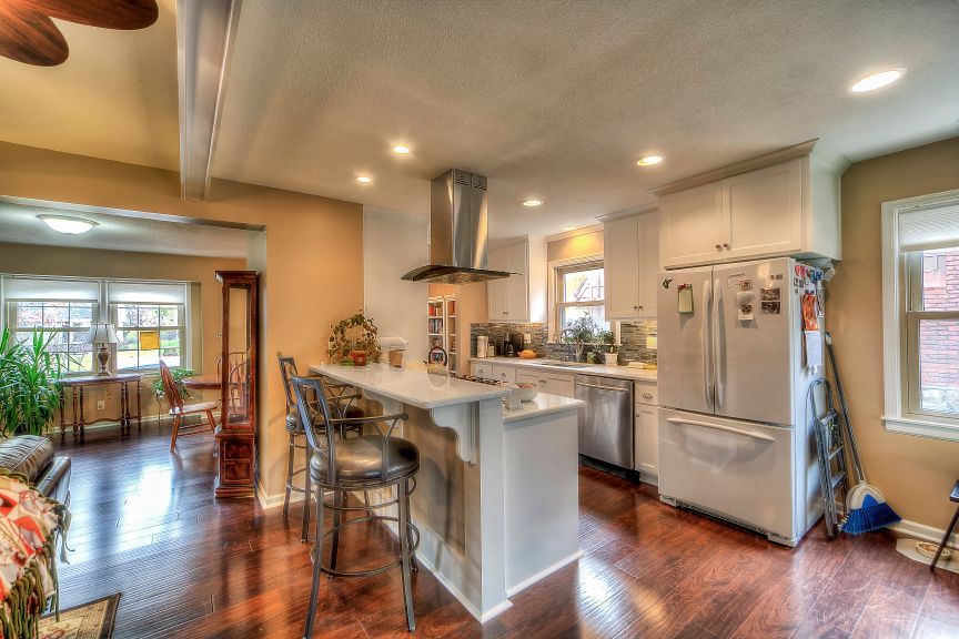 A kitchen with white cabinets , stainless steel appliances , a refrigerator and a ceiling fan.