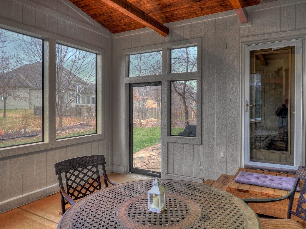 There is a table and chairs in the room with a lot of windows.