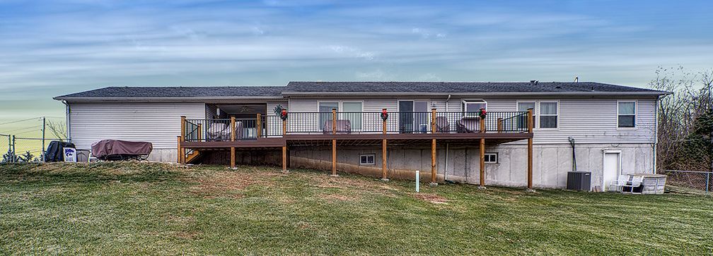 A large white house with a large deck is sitting on top of a grassy hill.