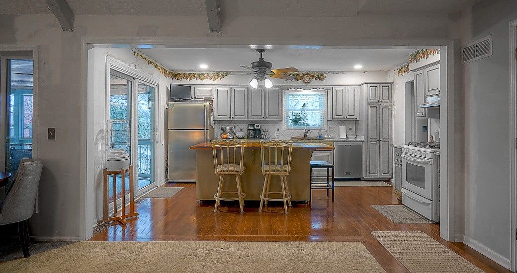 A kitchen with white cabinets , stainless steel appliances , hardwood floors and a large island.