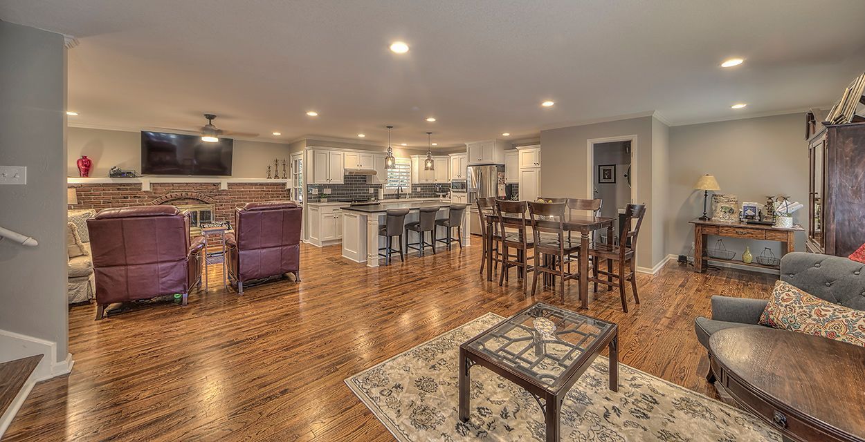 A living room with hardwood floors , a couch , chairs , a table and a television.