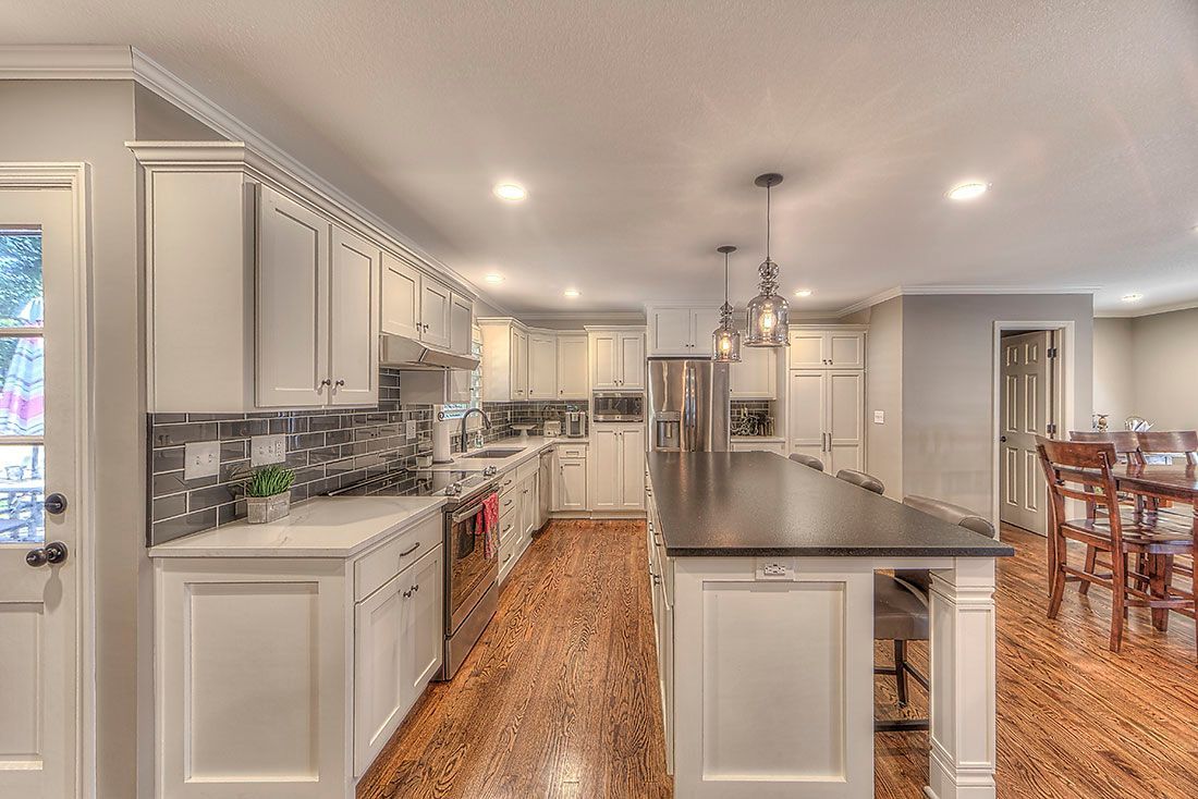 A kitchen with white cabinets , black counter tops , stainless steel appliances and hardwood floors.